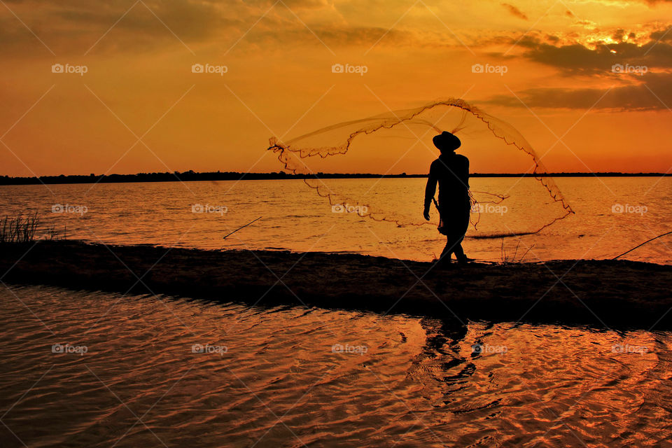 Fisherman throw nets under sunset at Galuh Cempaka Lake, South Kalimantan, Indonesia.