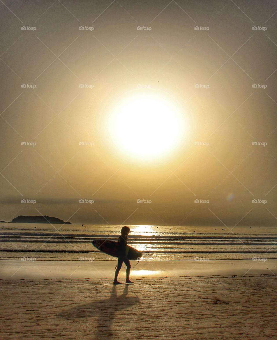 Surfer at sunset. Surfer walking along the beach in Essaouira, Morocco. 