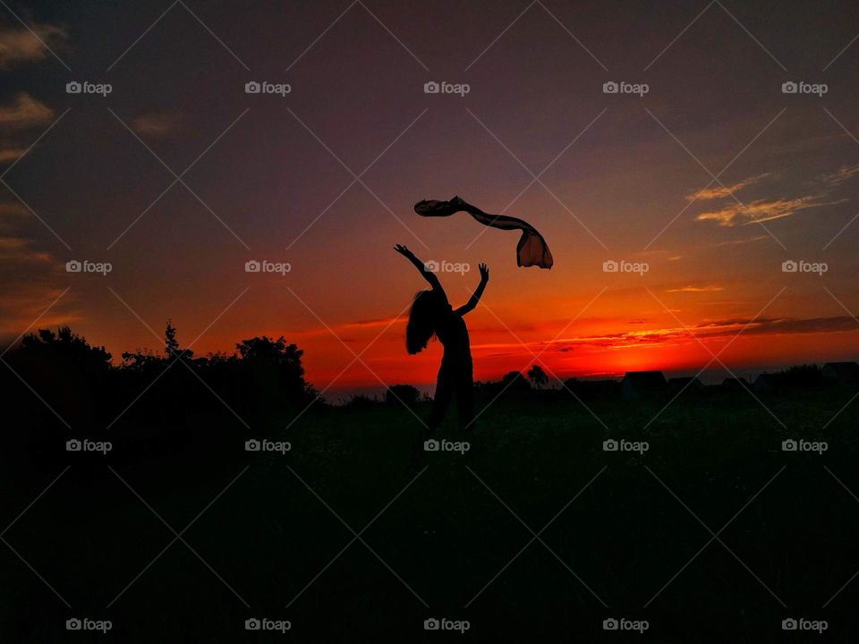 Girl playing with scarf. Silhouette on sky background