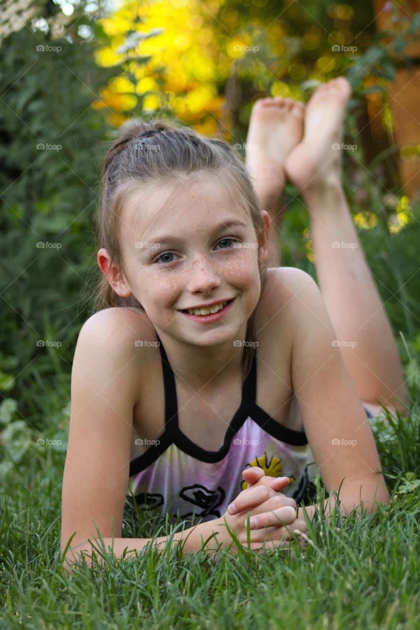 Preteen daughter smiling in the grass on a warm summer evening in the backyard 