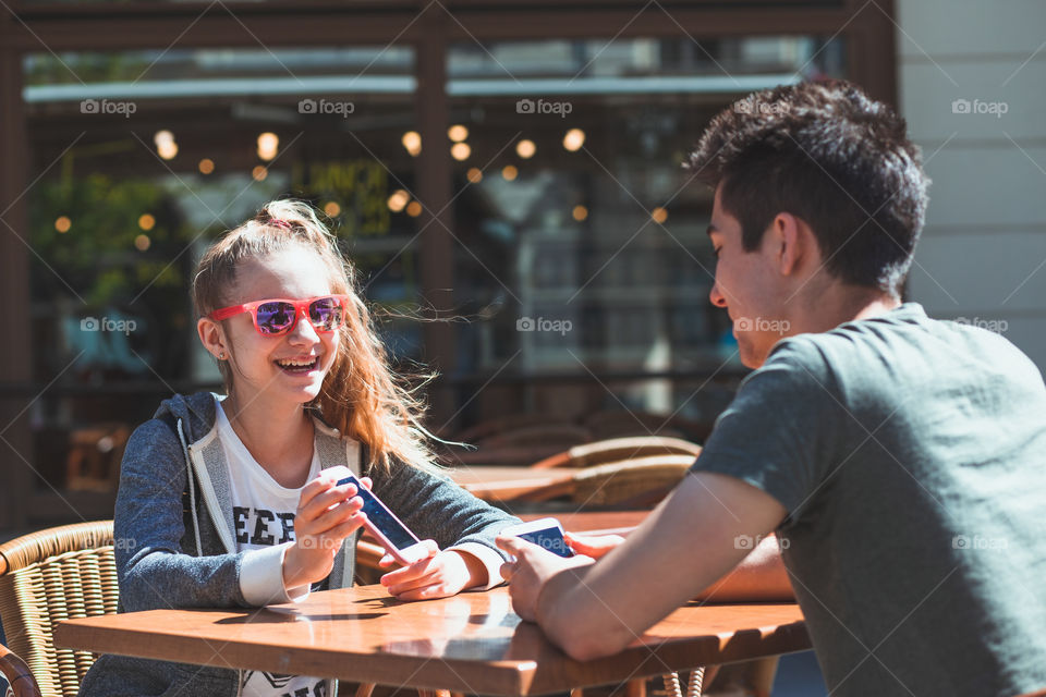 Young woman and man sitting in pavement cafe a the table talking and using mobile phones