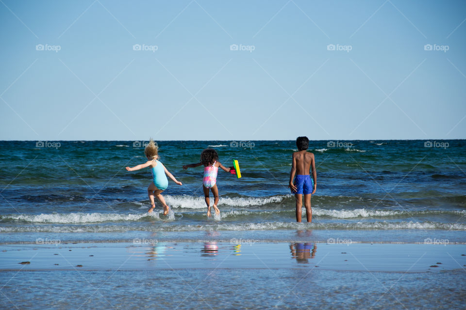 Young children jumping in the water at Höllviken beach in Sweden.