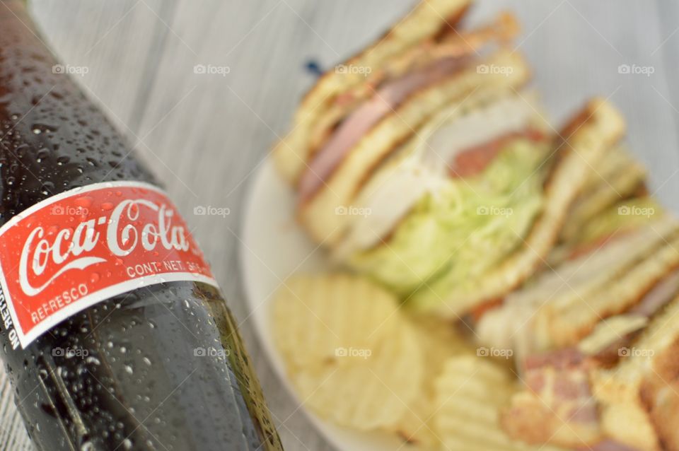 A Bottle of Coca Cola with a club sandwich on a white rustic background 