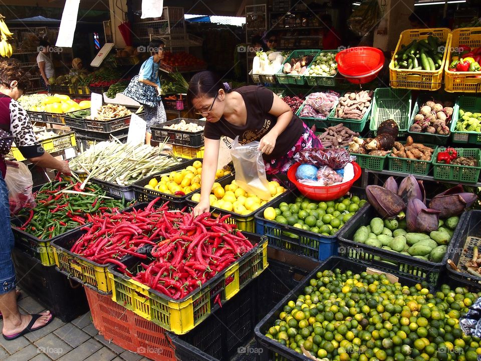 a lady buying fruits and vegetables at a market