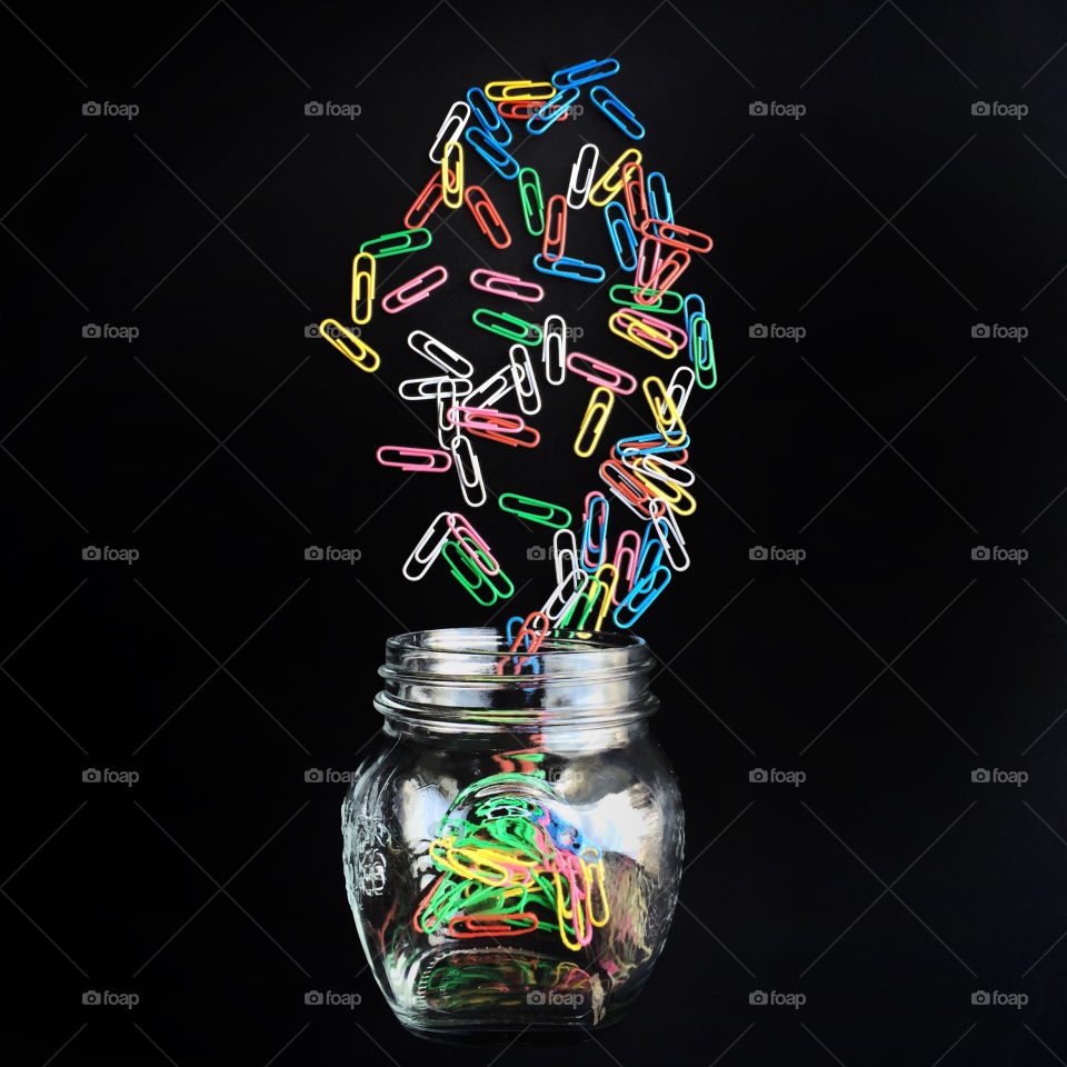 Colorful paper clips dropping into a glass
