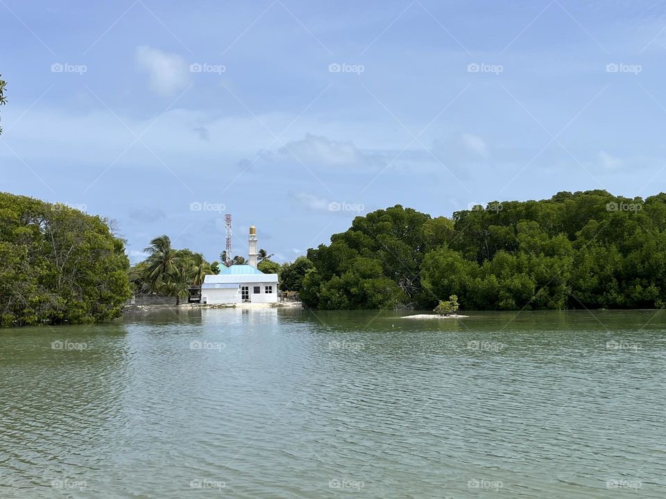 A small mosque on the beach side of Kaafu Huraa island in the Maldives is seen between its thick green tree line.
