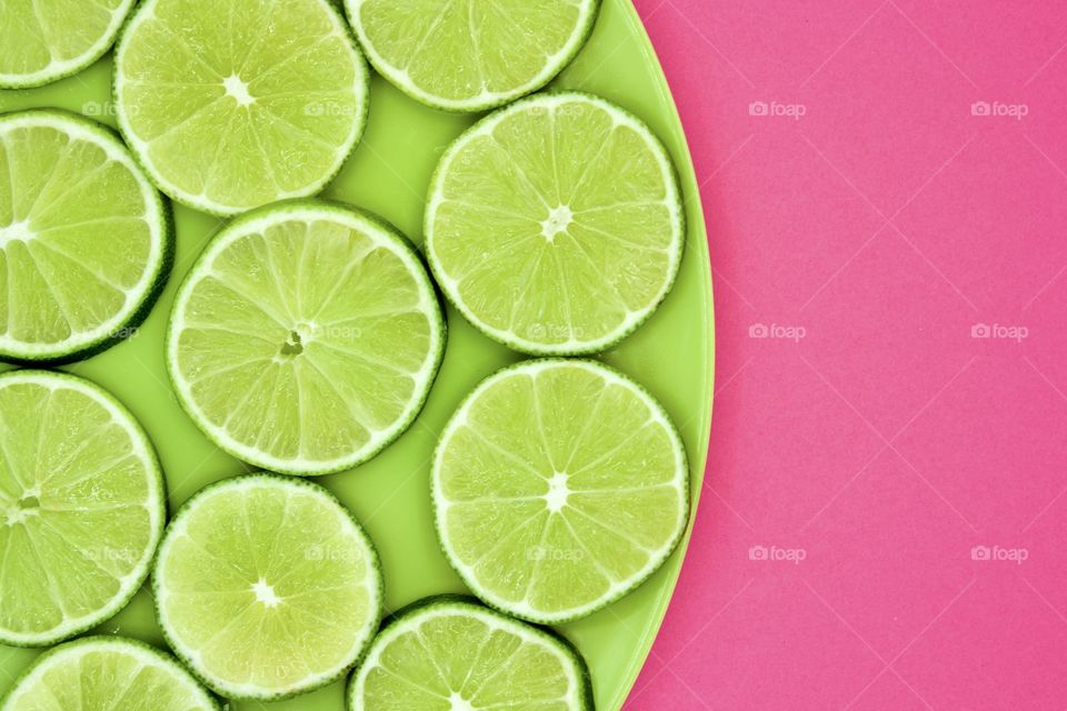 Minimalistic flat lay of lime slices on a green plate against a bright pink background