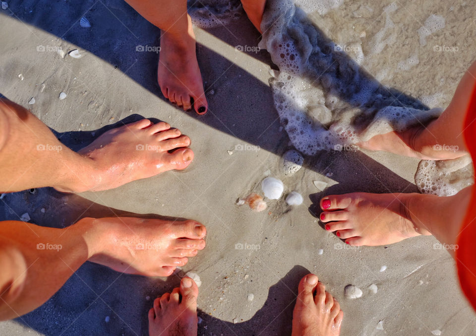 4 pair of feet on sandy beach with wave