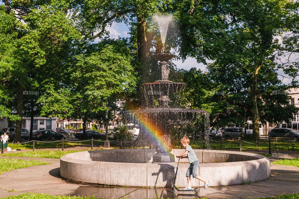 summertime, boy on the skate ride near fountain with rainbow