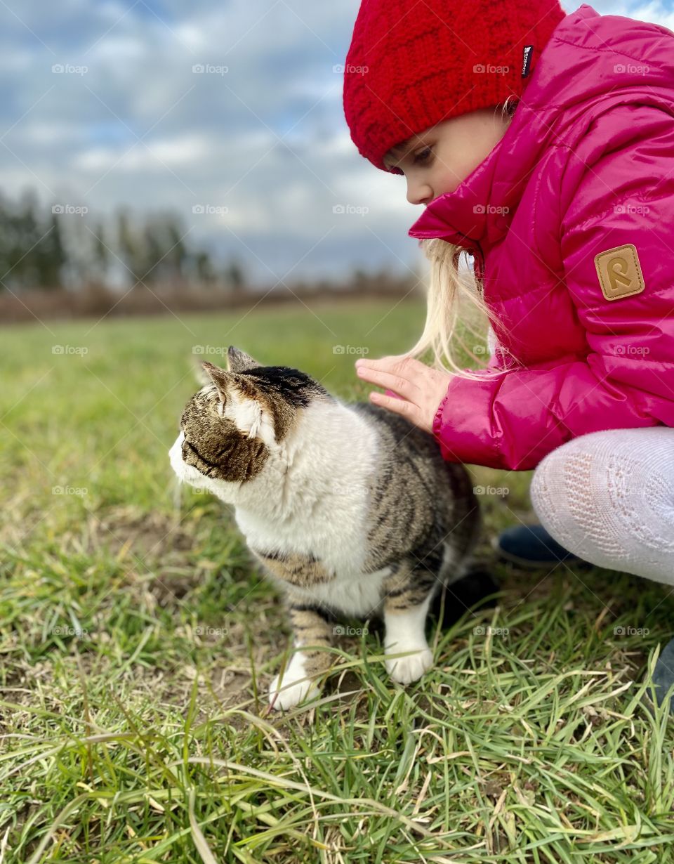 the cat sits on the grass, the girl hugs the cat