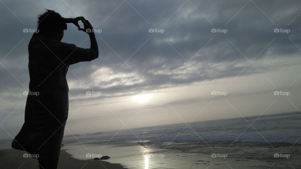 adult man draw heart by its hands and looking at the sunset.