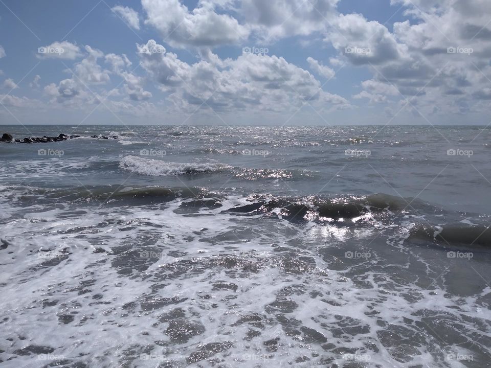 Picturesque view of the beautiful sea. Clouds are  floating in the sky. Waves splashing against the rocks.