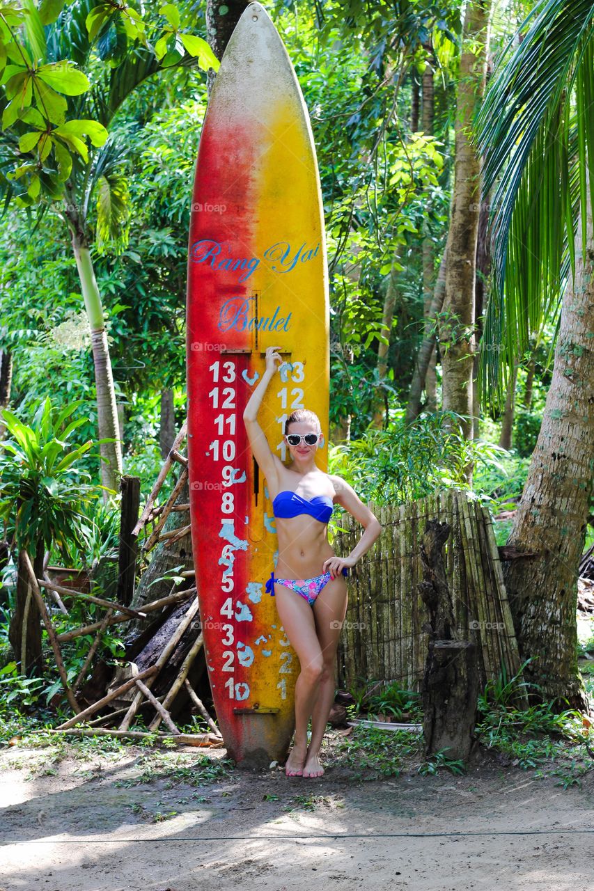 Woman in bikini standing near surf board