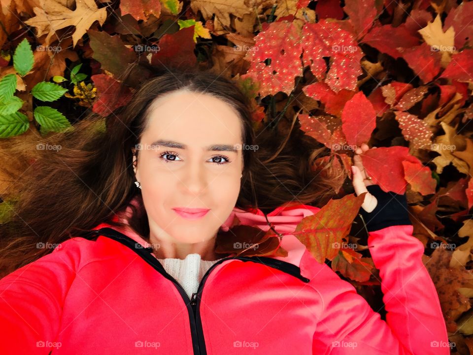 Portrait of young smiling woman surrounded by red and orange autumn leaves