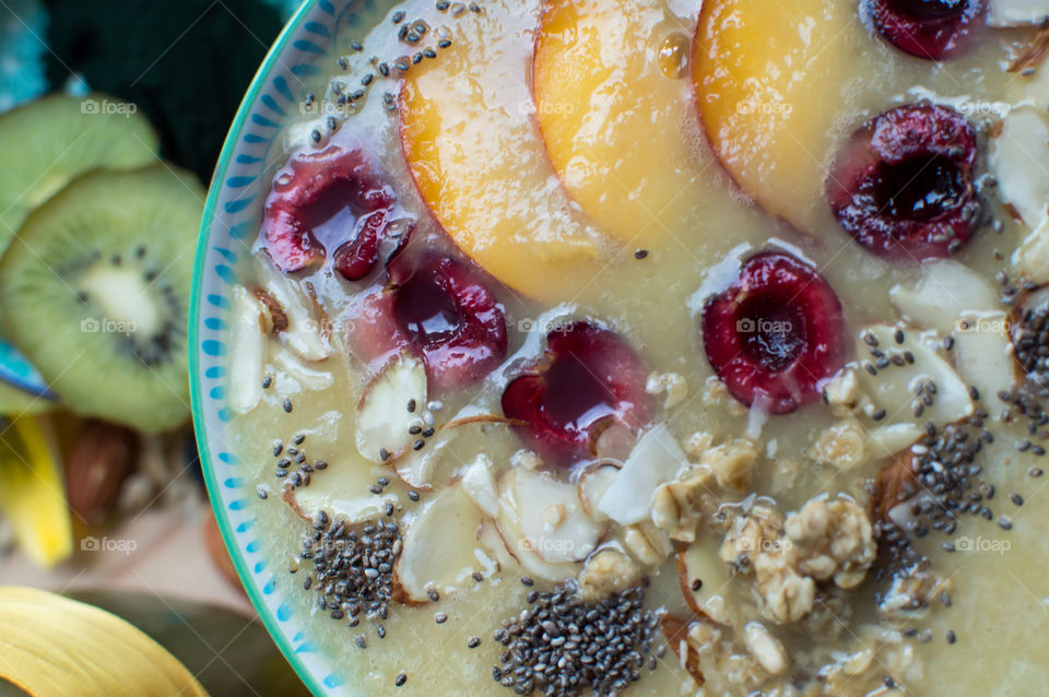 High angle view of beautiful artisanal smoothie bowl with freshly sliced peach, cherry, oatmeal, chia seed, almonds with elegant garnish elevated view with fruit and smoothie ingredients in background 