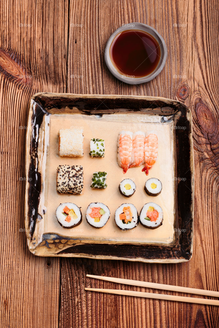 Sushi set on pottery plate with chopsticks and soy sauce in bowl on old wooden table from above