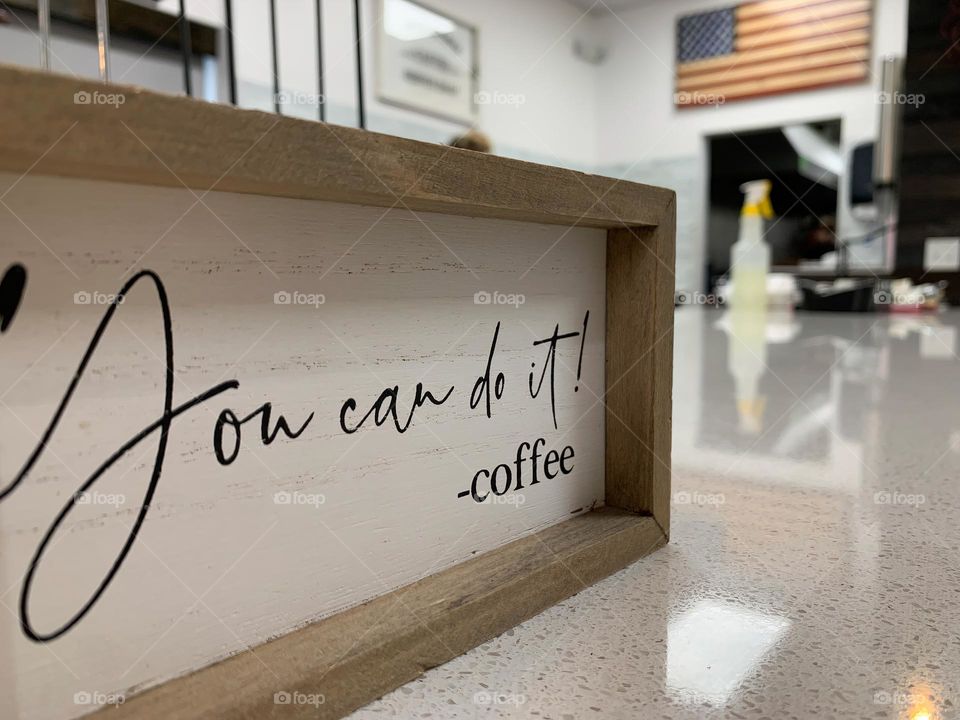 « You can do it! -coffee » sign in the foreground focus at a coffee shop interior small business unique brand seeing the coffee cups holder with the American flag on the background wall.