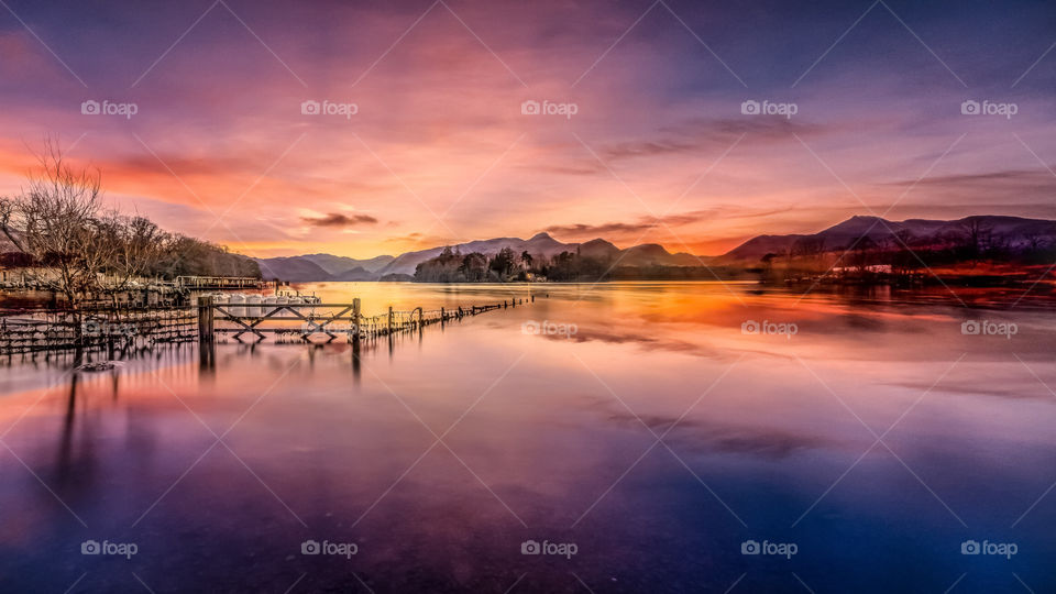 Flooded Fields And A Purple Sunset Photo
As the sun sets behind the distant mountains, it throws breathtaking hues of gold, purple and pink across the sky. The fields below have been flooded, and the fences and gates are partially hidden by the water
