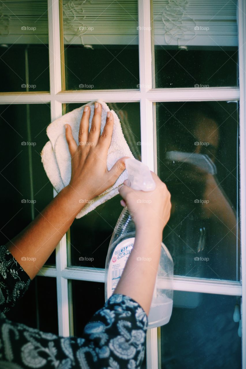 Young woman doing home cleaning. Daily chores and housework cleaning the glasses on door