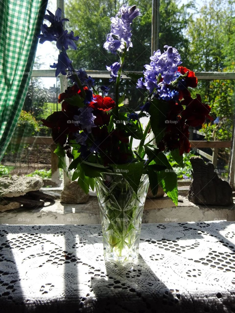 flowers in a vase next to the window with the sun shining on them