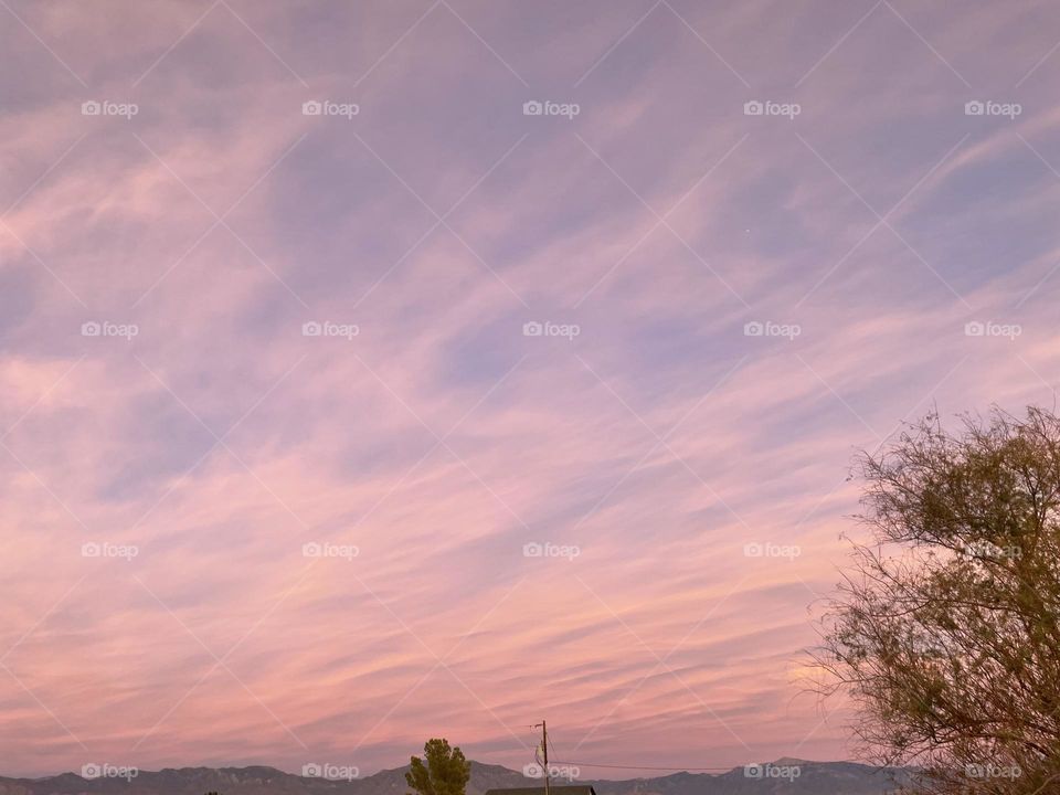 A photo of a sky full of beautiful pink clouds with mountains and trees. 