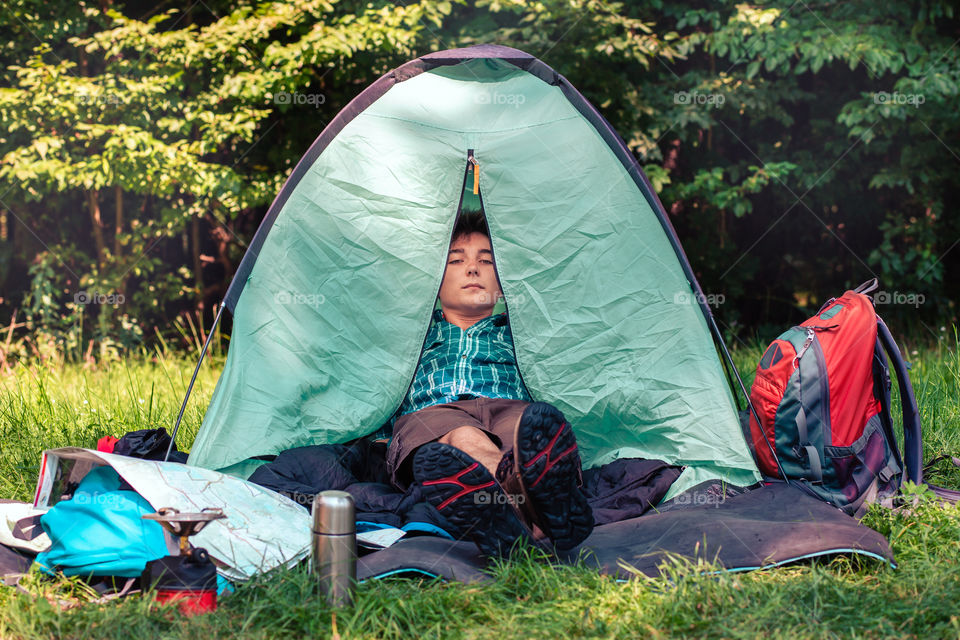 Spending a vacation on camping. Young man resting in a tent