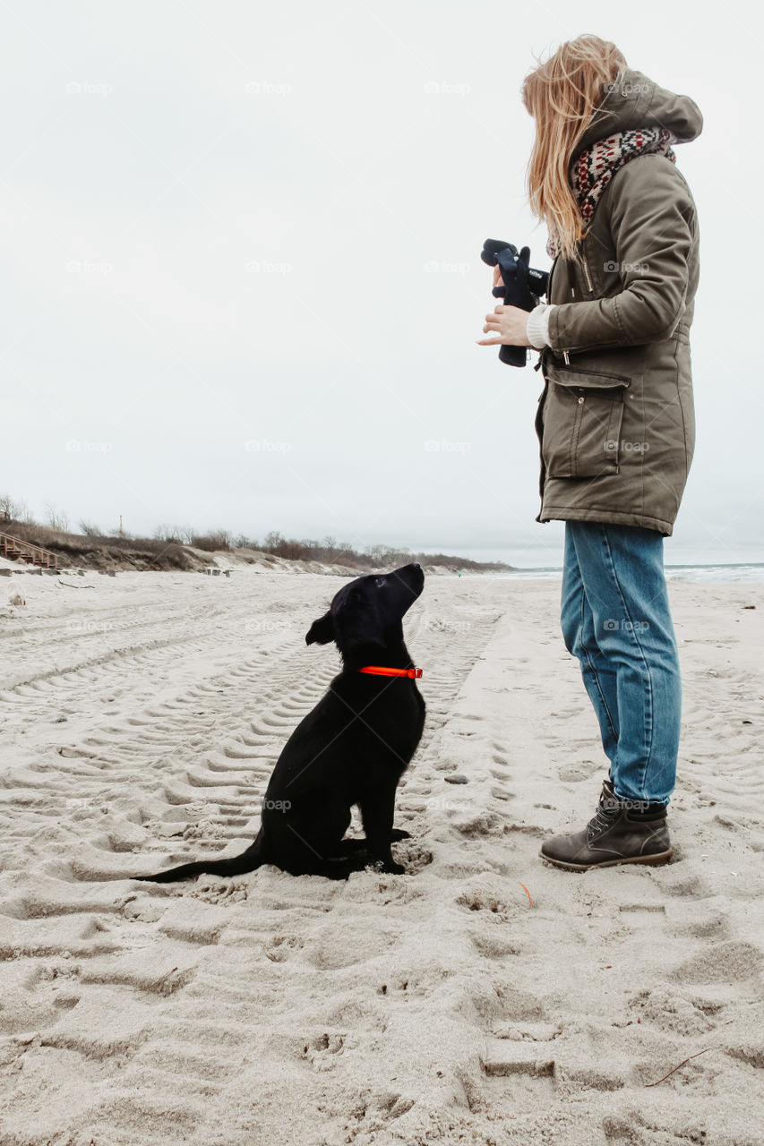 Girl is training her pet - black retriever puppy on a sandy beach