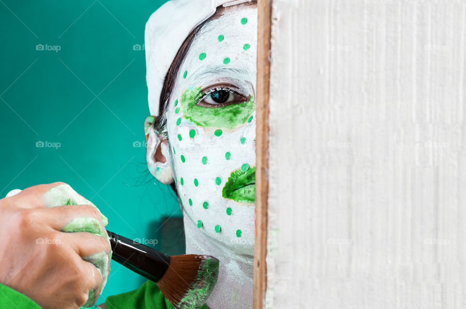 portrait of artist painting her face with green and white paint.