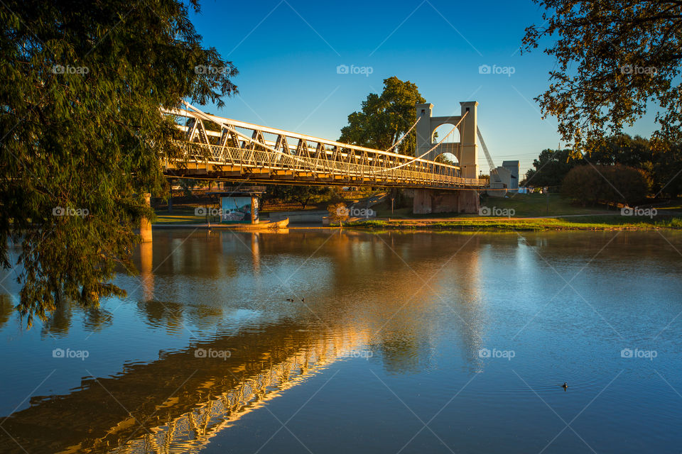 Built in 1870, this old historic suspension bridge crosses the Brazos River in Waco, Texas. This photo was taken along the waters edge at sunrise, capturing the structure as it was bathed in the golden glow of the morning sun
