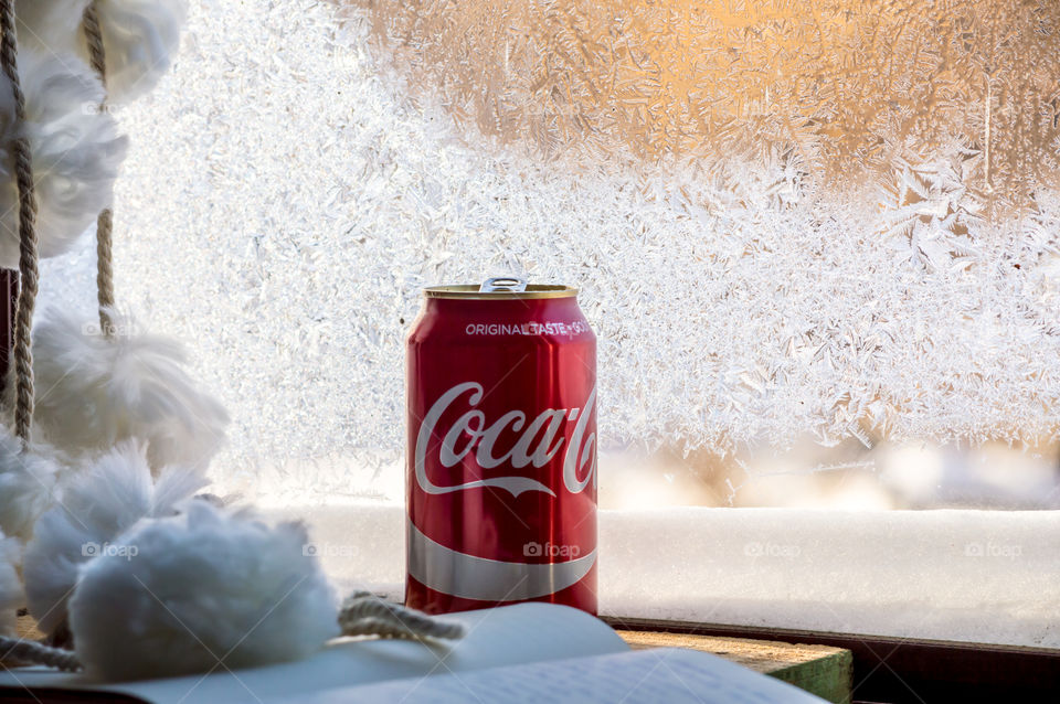 Red coke can on desk near sunny window covered with frost crystals on table with notebook and writing cozy winter indoors cool drink concept 