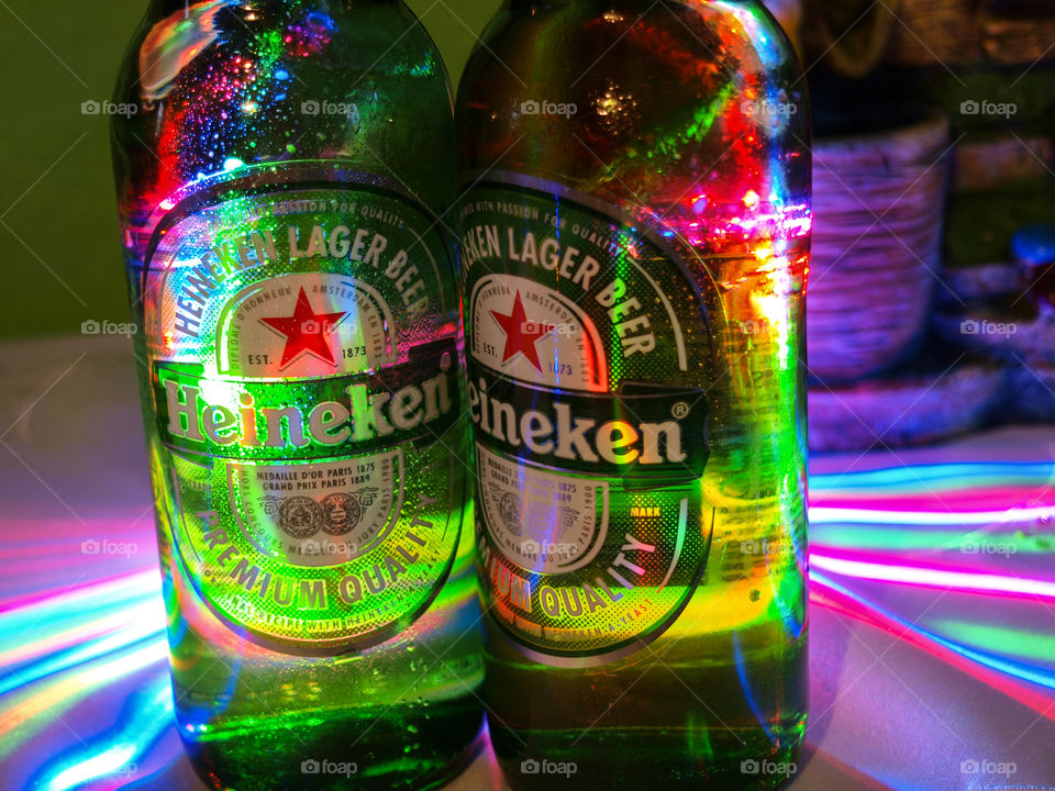 Colorful light illuminating Heineken bottles close up.