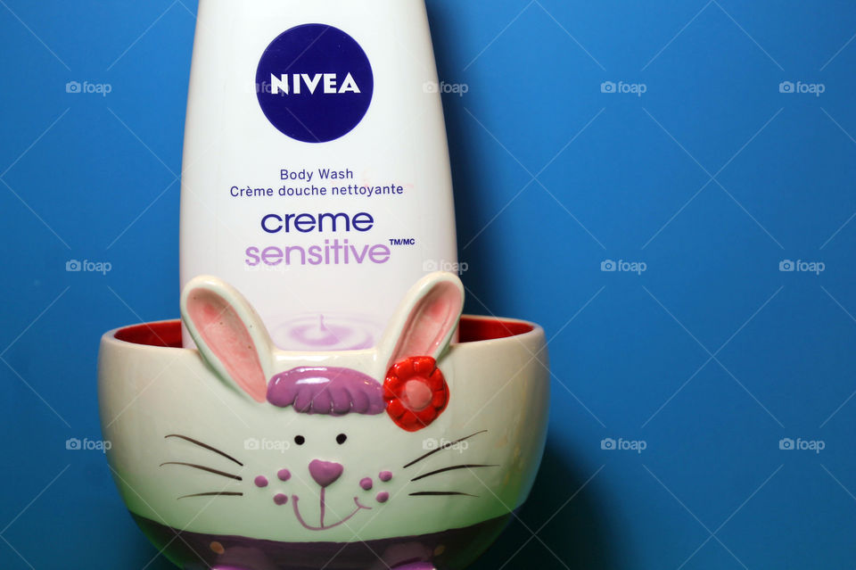 A white, purple and red Easter bowl is holding a bottle of NIVEA creme sensitive Body Wash and are set against an azure blue background. 