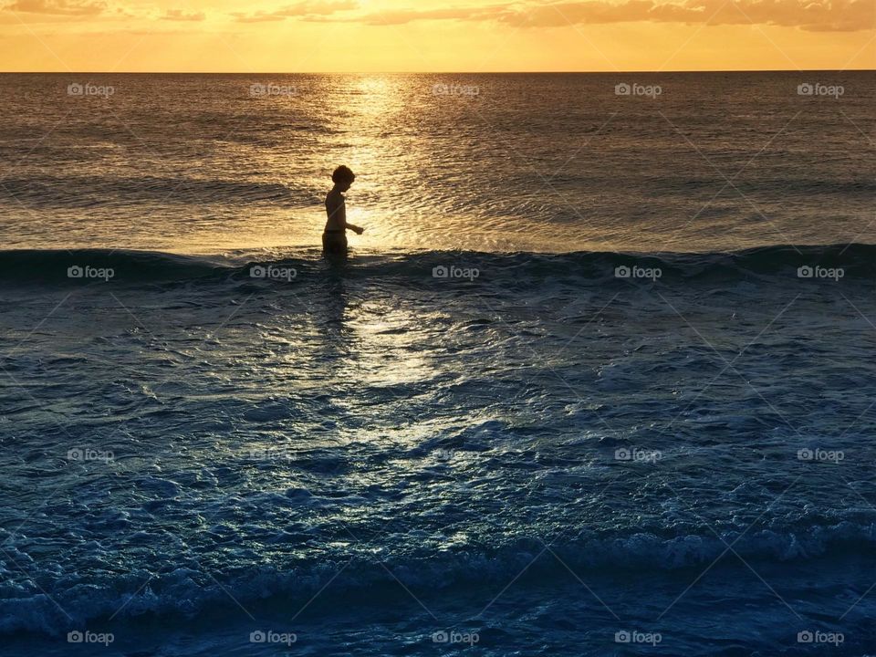 Small boy in the ocean glowing with summer sunlight .
