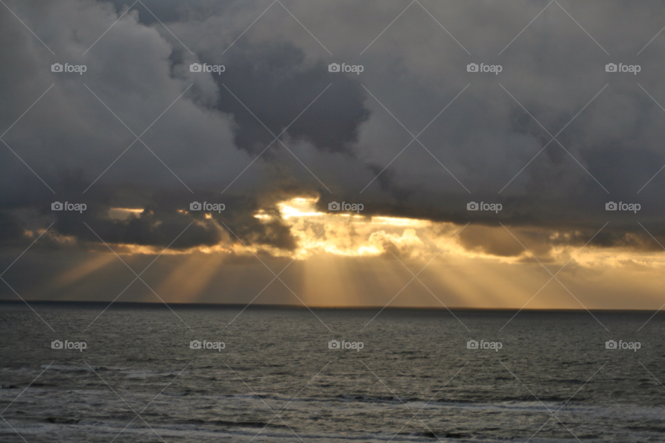 Sun rays over the ocean . Early evening clouds 