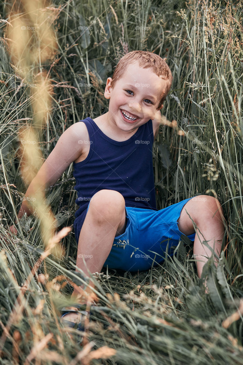 Little happy smiling kids playing in a tall grass in the countryside. Candid people, real moments, authentic situations