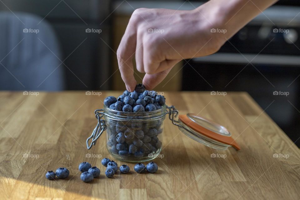 Hand takes blueberries from the glass jar 