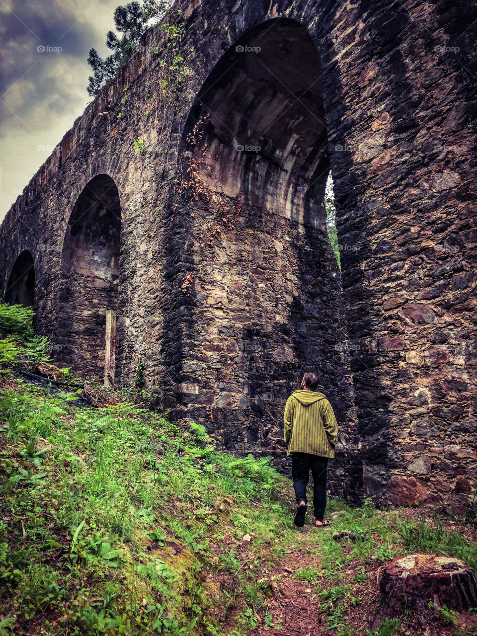 A man looks up in awe at the tall, ancient aqueduct arches that tower above him