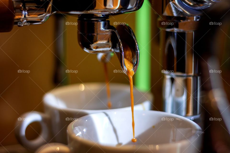 a closeup portrait of the nozzles of a coffee machine pouring coffee in two separate coffee cups.