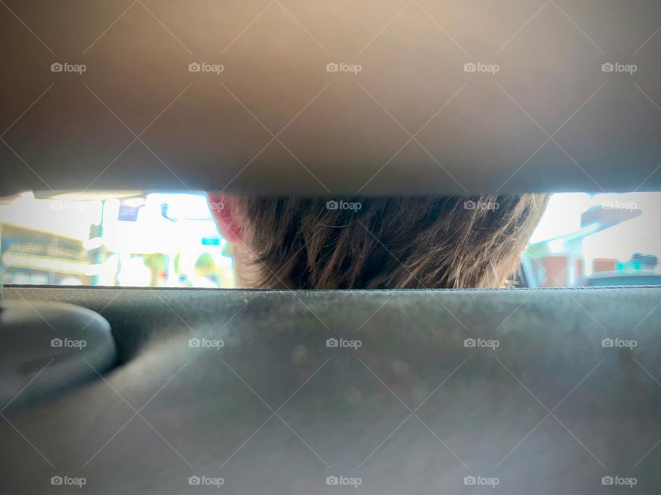 Commuting: teenager sitting on the front seat of a vehicle seeing the back of his head through the crack between the head rest and the chair, close-up.