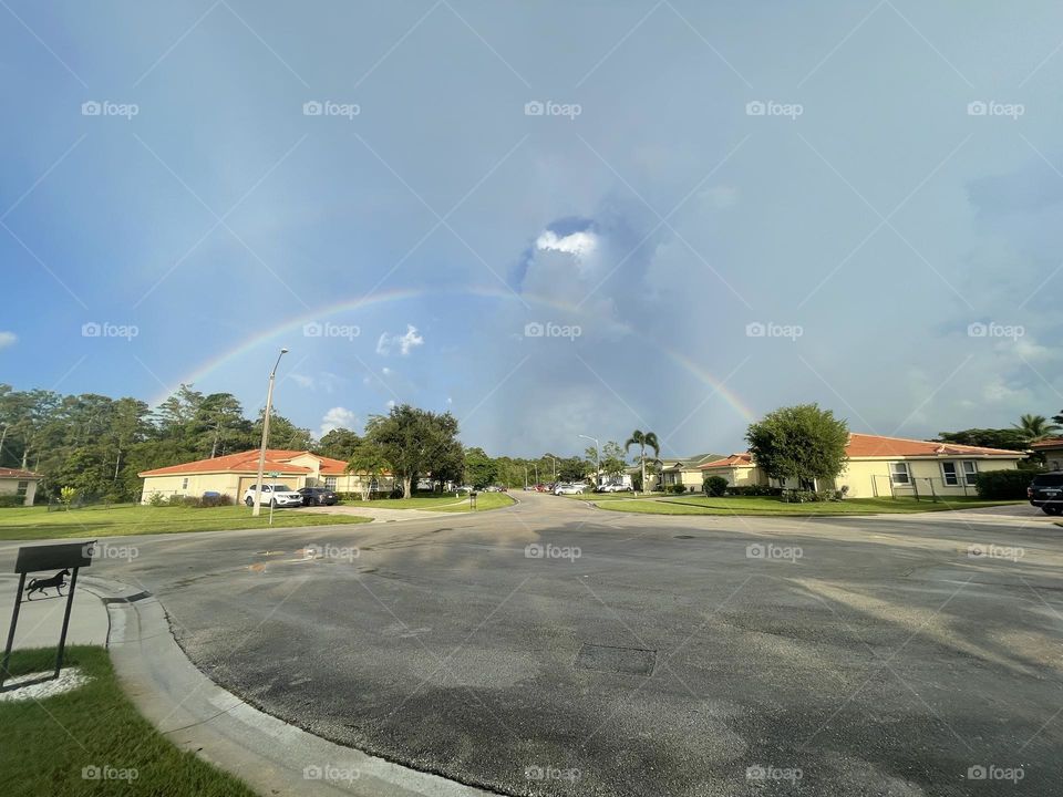 A rainbow glows over a Florida neighborhood. The rainbow goes from one side of the sky to the other.