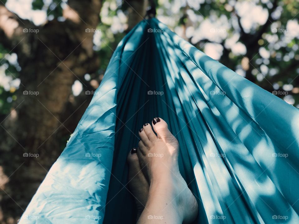 Person laying down in the hammock in the shadowing tree