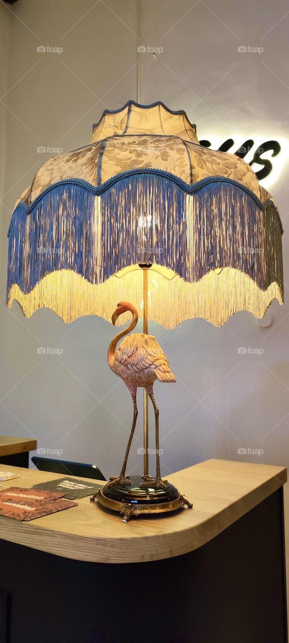 A beautiful “Tiffany” style lamp featuring a graceful pink flamingo next to the stand welcomes all guests at a popular bar and restaurant in “Regensburg”, a city at the northernmost section of the “Danube”. 2023. Hypnotic Productions