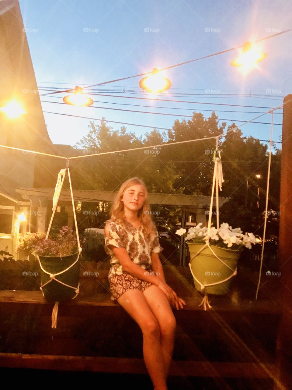 This is a beautiful photo at dusk with a pretty girl with fairy lights and flowers