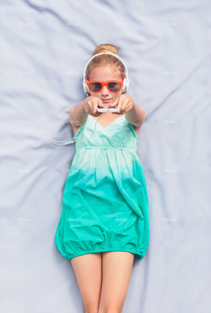 Teenage girl in headphones lying on bed