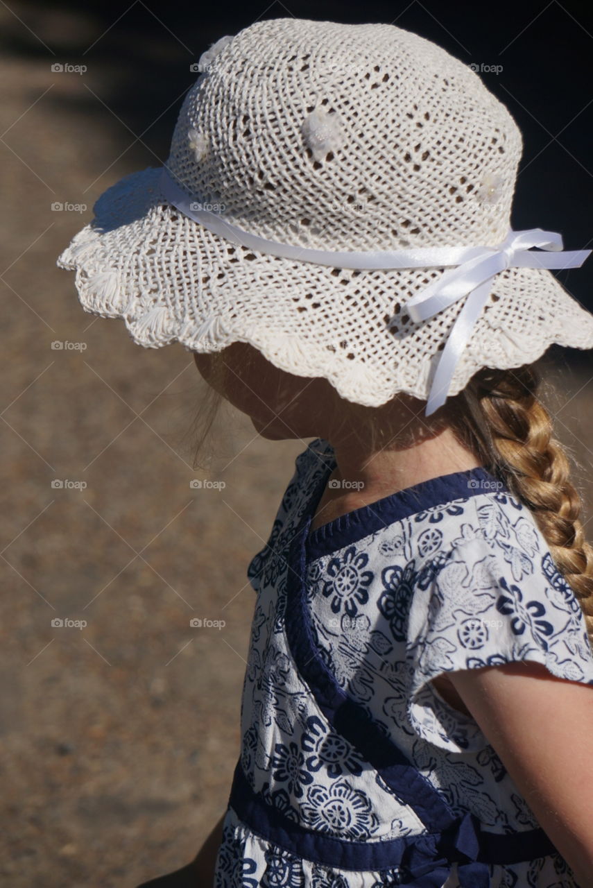 Little girl with a braid and wearing a hat and dress