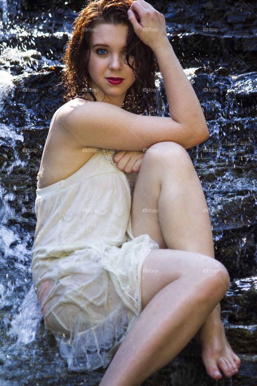 Portrait of a young woman sitting on waterfall