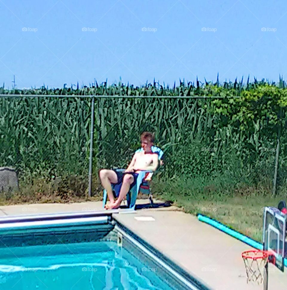 Boy sitting by pool in a corn field.