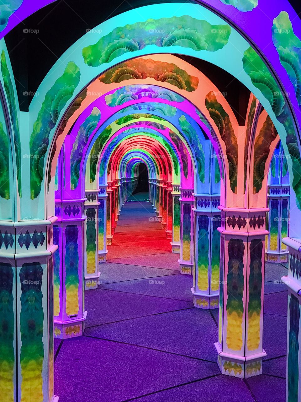 Hall of mirrors with arches lit up and reflecting the colors of the rainbow giving the allusion of a vast space 