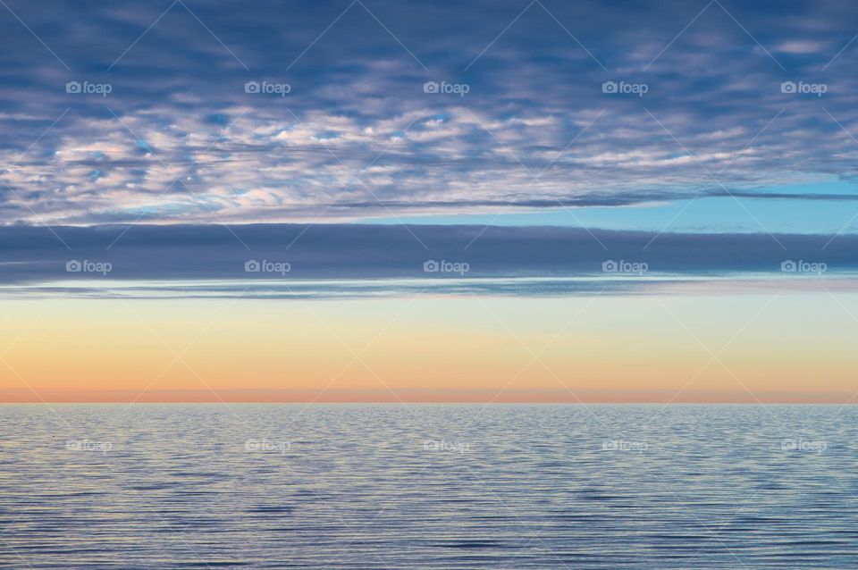 Blue and yellow cloud lines in the sunset sky over the sea