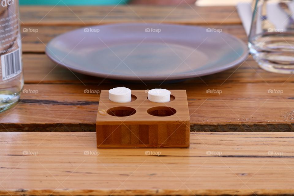 Two rolled up napkin serviettes that expand with water in wood container on wood outdoor restaurant table, pottery plate, rustic modern blur background
